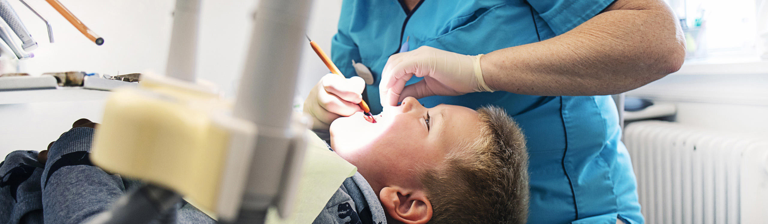 A child is lying in a dental chair while a dentist examines their mouth, using a light and dental tools.